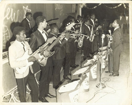 (Front with trombone) Carlos Malcolm and His Afro-Jamaican Rhythms at the Glass Bucket Club, Kingston Jamaica. (Left to right) Bunny Cameron- electric guitar, Boris Gardner- electric bass/singer, Ozwald Lawson- trumpet, Winston Turner (hidden)- trumpet, Les Samuels (hidden)- tenor saxophone, Carl “Cannonball” Bryan- alto saxophone, Lascelles Perkins- singer. (Left to right in background) Winston 'Sparrow' Martin- drummer, Alphonso Castro- Lt. percussion.